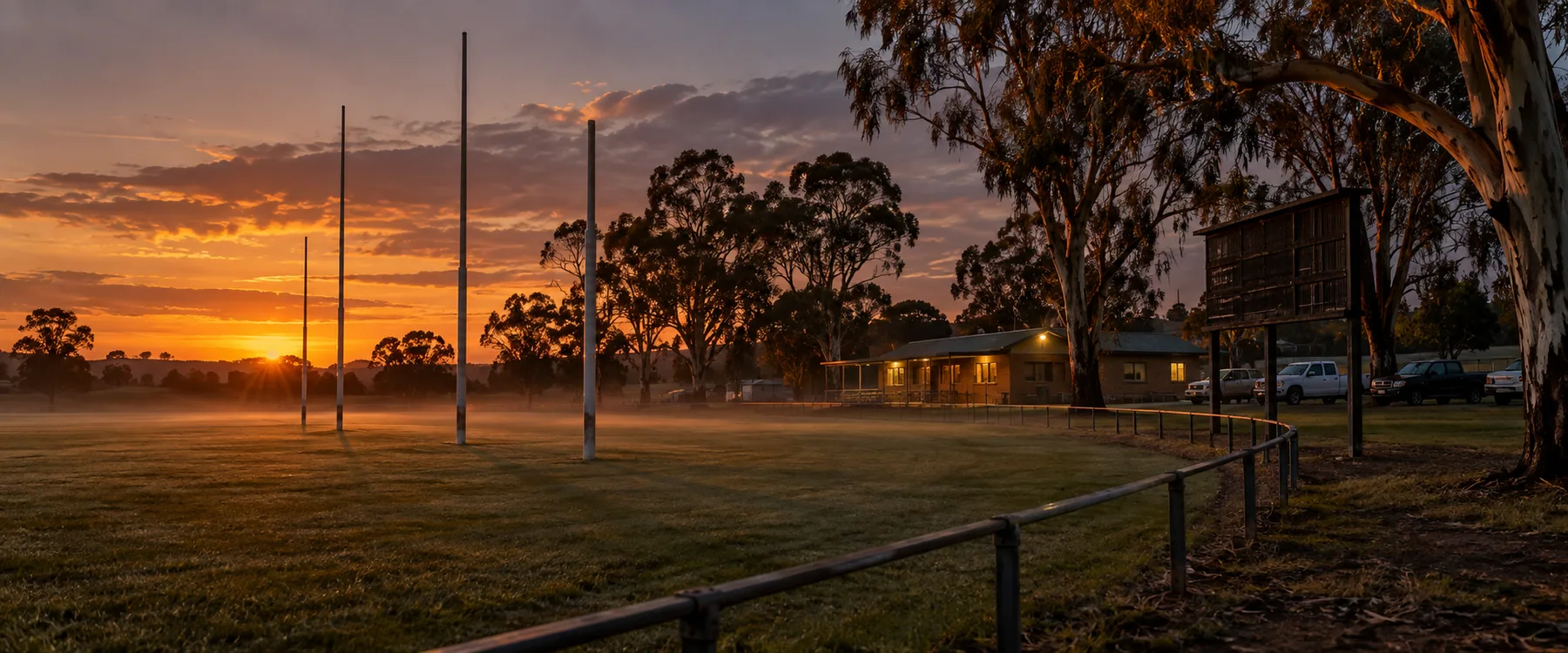 A country football oval at dusk with the goal posts lit against the sky